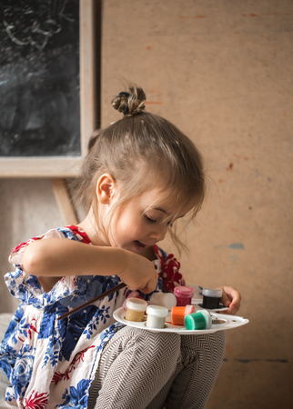 a little girl with colours in hands on the background of the easelの写真素材