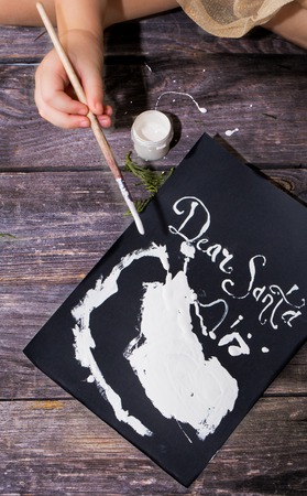 Beautiful cute little girl writes letter to Santa near Christmas decoration on the wooden floorの写真素材