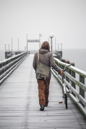 a single man dressed in old clothes on the embankment with the bikeの写真素材