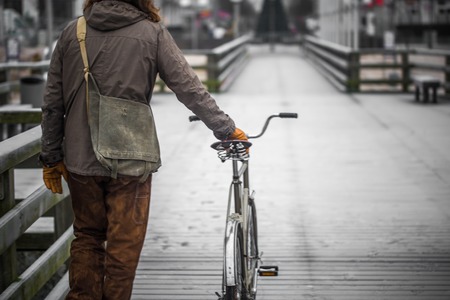 a single man dressed in old clothes on the embankment with the bikeの写真素材