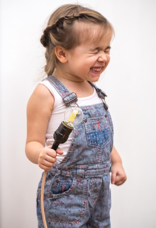 little cute girl with light bulb in hand sitting on the Hank of wires for electricians,concept ideasの写真素材