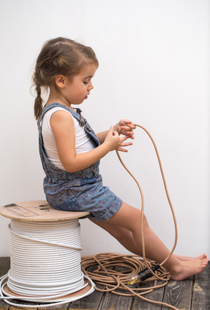 little cute girl with light bulb in hand sitting on the Hank of wires for electricians,concept ideasの写真素材