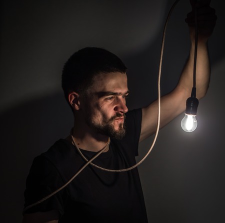 a young man holding a burning light bulb in hand on black background concept ideasの写真素材