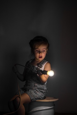 little cute girl with light bulb in hand sitting on the Hank of wires for electricians,concept ideasの写真素材