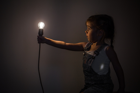 little cute girl with light bulb in hand sitting on the Hank of wires for electricians,concept ideasの写真素材