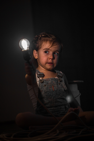little cute girl with light bulb in hand sitting on the Hank of wires for electricians,concept ideasの写真素材