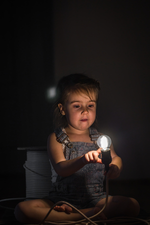 little cute girl with light bulb in hand sitting on the Hank of wires for electricians,concept ideasの写真素材