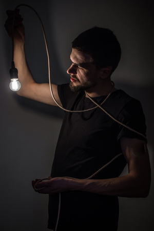 a young man holding a burning light bulb in hand on black background concept ideasの写真素材