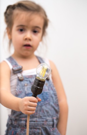 little cute girl with light bulb in hand sitting on the Hank of wires for electricians,concept ideasの写真素材