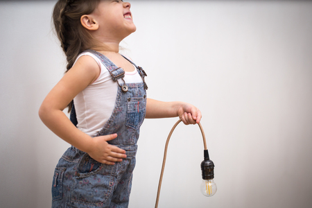 little cute girl with light bulb in hand sitting on the Hank of wires for electricians,concept ideasの写真素材