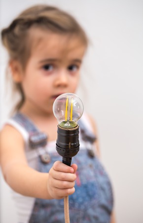 little cute girl with light bulb in hand sitting on the Hank of wires for electricians,concept ideasの写真素材