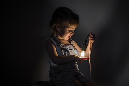 little cute girl with light bulb in hand sitting on the Hank of wires for electricians,concept ideasの写真素材