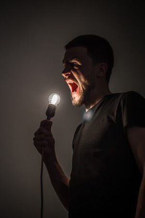 a young man holding a burning light bulb in hand on black background concept ideasの写真素材