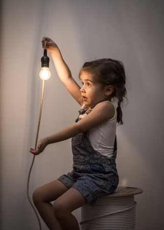 little cute girl with light bulb in hand sitting on the Hank of wires for electricians,concept ideasの写真素材