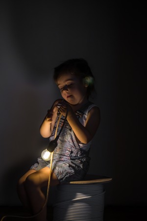 little cute girl with light bulb in hand sitting on the Hank of wires for electricians,concept ideasの写真素材