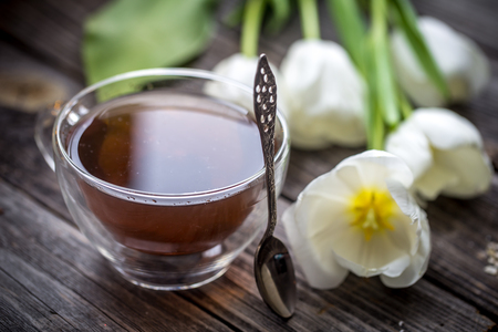beautiful white tulips and a transparent Cup of tea on wooden background, holiday conceptの写真素材