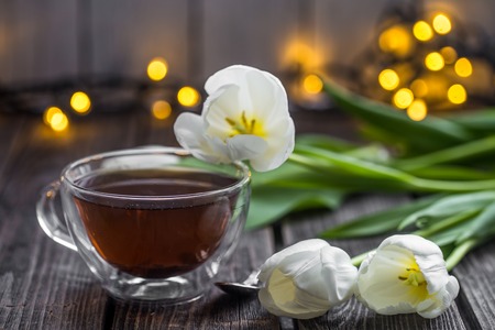 beautiful white tulips and a transparent Cup of tea on wooden background, holiday conceptの写真素材
