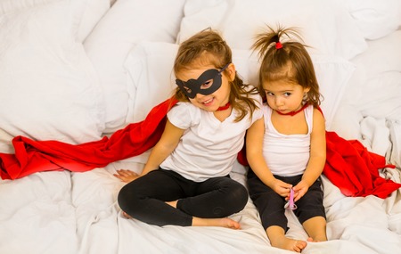two little girls play costumes super-hero sitting on a white bed,the concept of leadership,victoryの写真素材