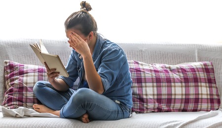 White cozy bed and beautiful girl reading a book, place for text, concept of home and comfortの写真素材