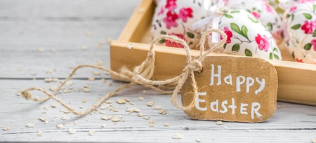 Easter composition with eggs fabric flower in a wooden box and the words happy Easter is on a light wooden backgroundの写真素材