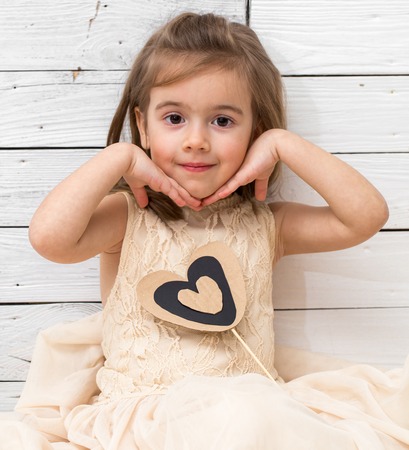 little cute girl in dress sitting on white wooden background with a heart in his hands, holiday conceptの写真素材