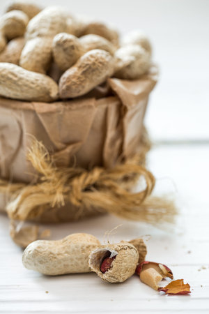 Unshelled peanuts closeup on white wooden background, concept of healthy nutrition