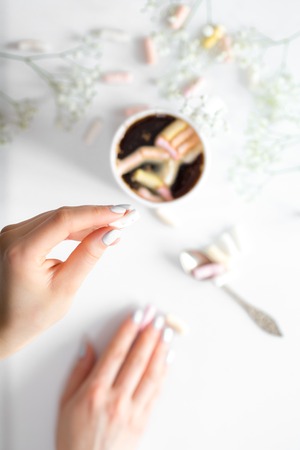 White coffee Cup with colorful marshmallows and small flowers with female hands on white background ,concept of drinks and relaxの写真素材