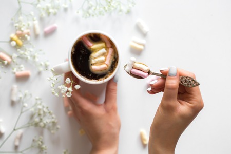 White coffee Cup with colorful marshmallows and small flowers with female hands on white background ,concept of drinks and relaxの写真素材