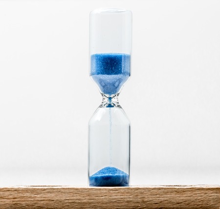 Glass hourglass with blue sand , closeup on white background, time conceptの写真素材