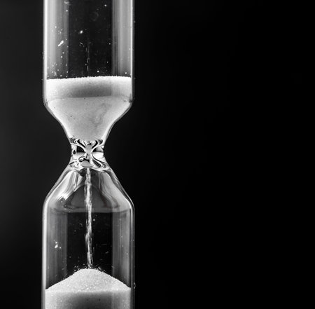 Glass hourglass with white sand , closeup on black background, time concept