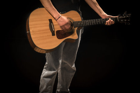 young man with acoustic guitar on black background, creative musical concept