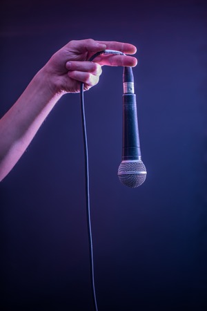 hand with microphone on a black background, the music concept, beautiful lighting on the stage, closeupの写真素材