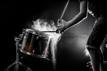 man plays musical percussion instrument with sticks closeup on a black background, a musical concept with the working drum, beautiful lighting on the stageの写真素材