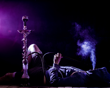 a man smokes a hookah on a black background, holiday concept, beautiful lightingの写真素材
