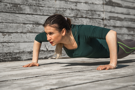 fitness sporty girl in sporty clothes is doing exercises on a wooden background, light background ,the concept of sportsの写真素材
