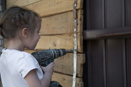 Little girl with screwdriver in hands tightening bolts on wooden background,closeupの写真素材