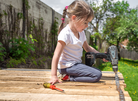 little girl outdoors repairing with screwdriver and wrench in hand, tightening bolts on a wooden background,closeup, concept of repairの写真素材