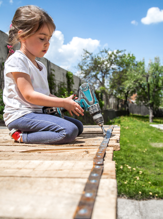 little girl outdoors repairing with screwdriver and wrench in hand, tightening bolts on a wooden background,closeup, concept of repairの写真素材