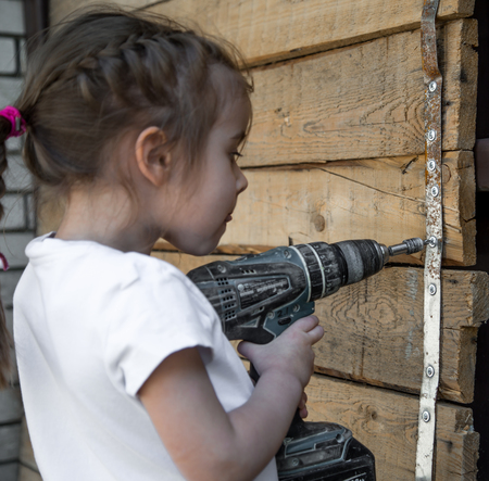 Little girl with screwdriver in hands tightening bolts on wooden background,closeupの写真素材