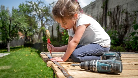little girl outdoors repairing with screwdriver and wrench in hand, tightening bolts on a wooden background,closeup, concept of repairの写真素材