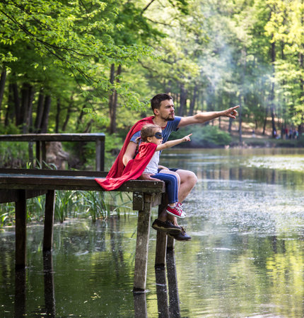 Happy loving family, father and daughter playing a super hero in the open air near the river on the wooden pier,the concept of a super hero and a child's dreams,father's Dayの写真素材