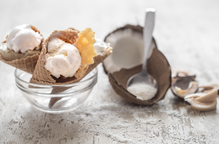 Vanilla-coconut ice cream in a waffle cone in a transparent glass bowl on wooden background with coconuts,the concept of ice creamの写真素材