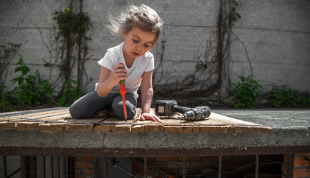 little girl outdoors repairing with screwdriver and wrench in hand, tightening bolts on a wooden background,closeup, concept of repairの写真素材
