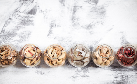 Different nuts in small jars on a light wooden background, a concept of healthy foodの写真素材