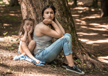 Sad emotions of a little girl with her mother near the tree in the park, the concept of family...