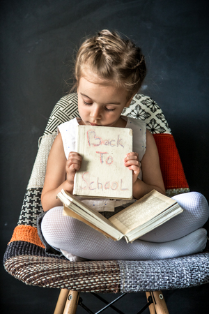 little girl sitting on a chair and reading a bookの写真素材
