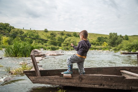 A little boy with a fishing rod fishing in a wooden boat ,the concept of fisheriesの写真素材