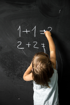 Cute girl schoolgirl near blackboard with chalk in hand,the concept of education and school lifeの写真素材