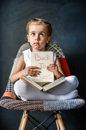Cute little girl sitting on a beautiful chair with a book in hand,the concept of education and school lifeの写真素材