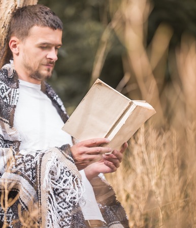 Young stylish handsome man at the tree reading a book, the concept of rest and readingの写真素材